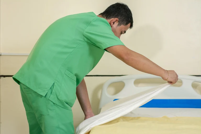 A student fits a fresh sheet on a bed